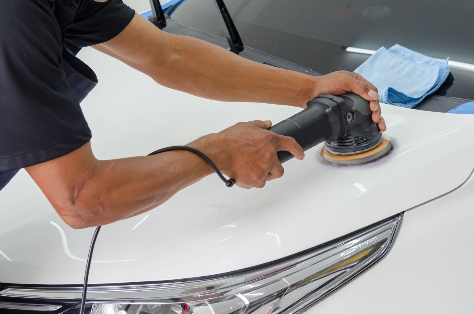 A detailer using a dual-action polisher on a car's paint, with a microfiber towel nearby