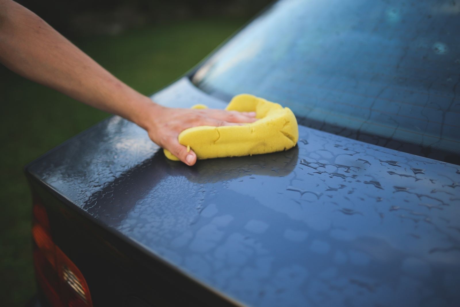 A hand washing a car's hood with a sponge, wet paint beading