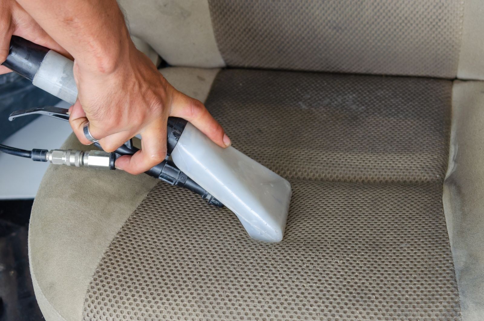 Hands using a steam extractor tool to deep clean a car's fabric seat